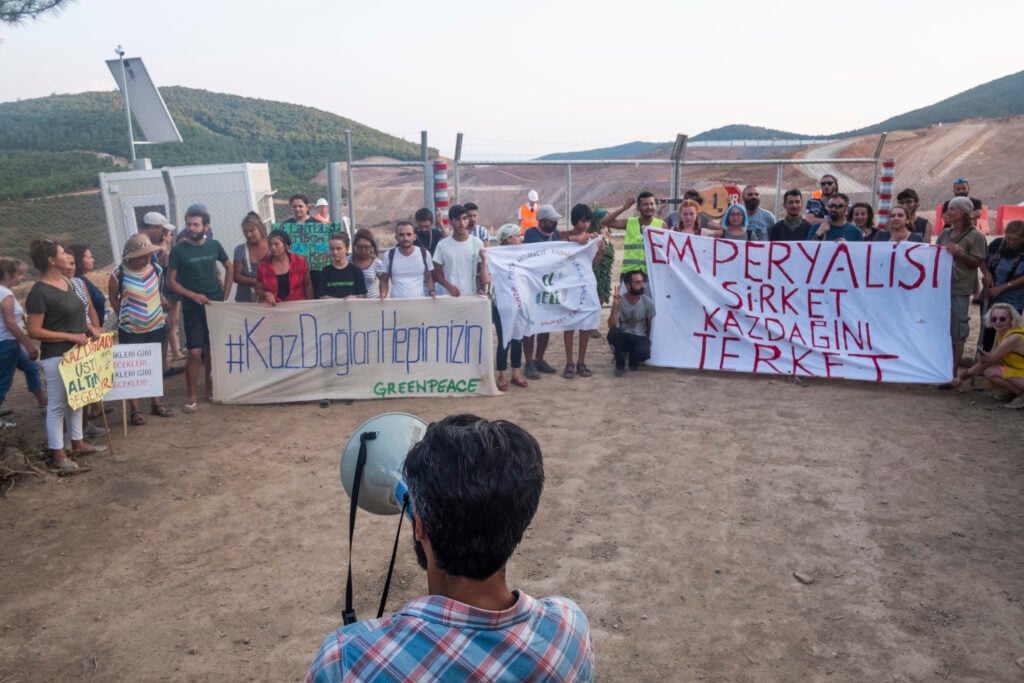 Protesters at the entrance of the Kirazli gold mine in Türkiye. One of the has a megaphone, and they hold banners.